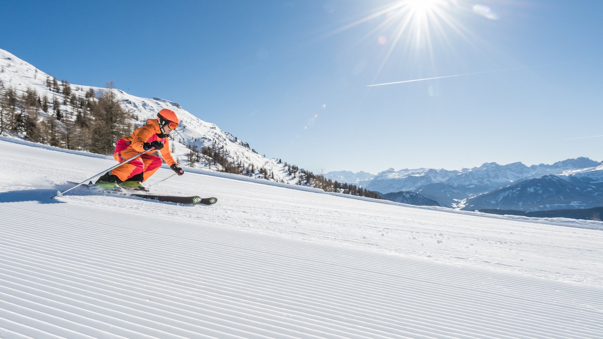 Child skiing on groomed slope on sunny day with mountains in the background