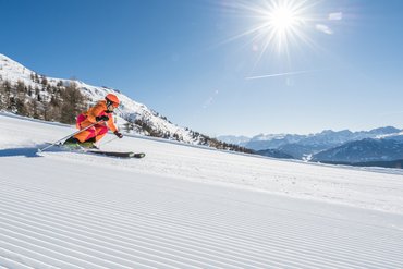 Child skiing on groomed slope on sunny day with mountains in the background