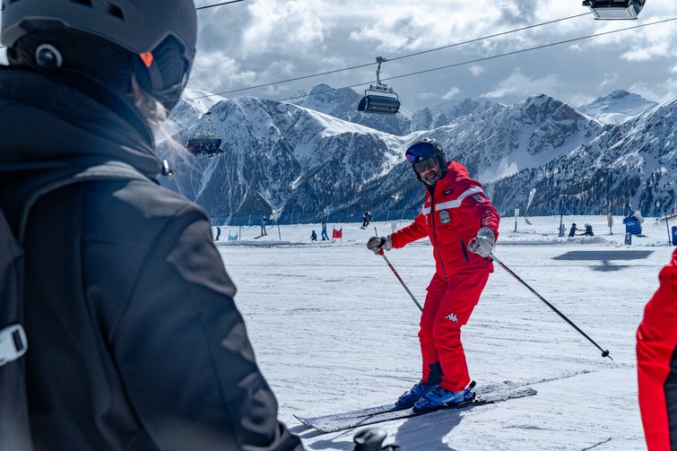 Skilehrer in rotem Anzug zeigt Skifahrer Technik auf verschneiter Piste