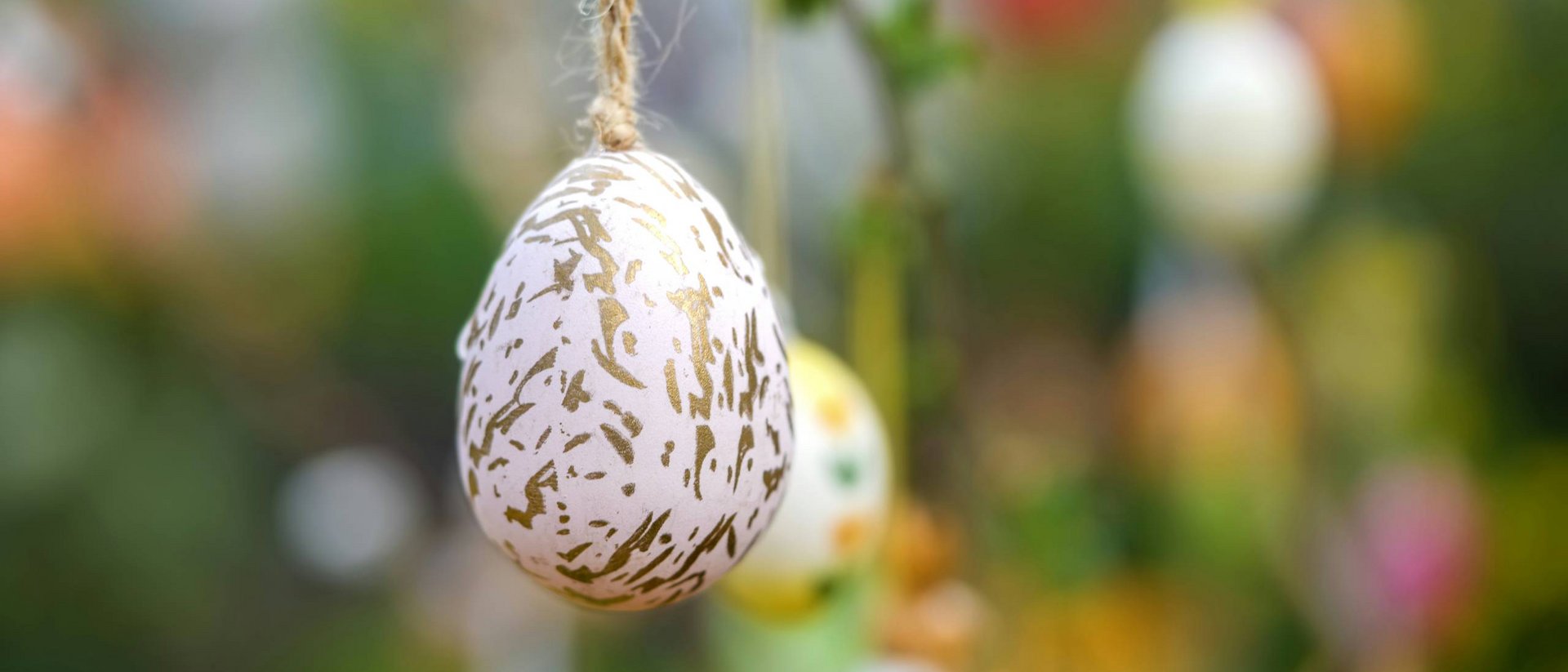 Osterei mit goldenem Muster hängt an Faden vor unscharfem Hintergrund