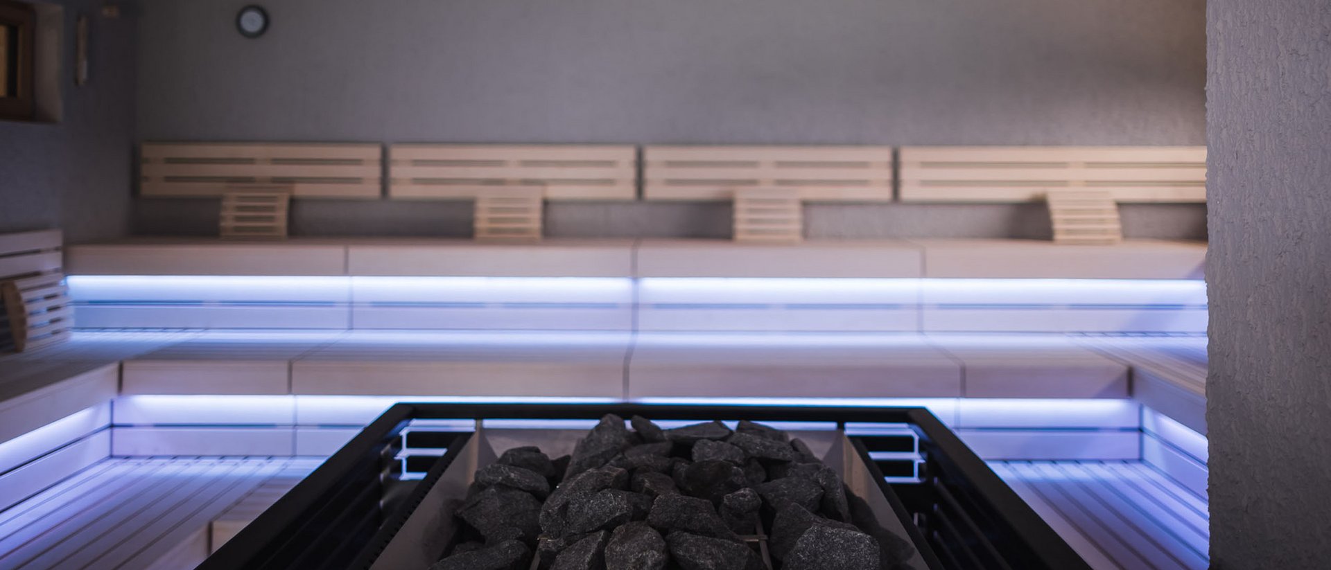 Sauna moderna con panche in legno illuminate e pietre nella stufa