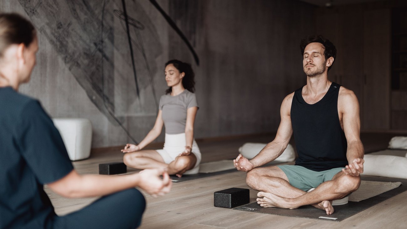 Personen meditieren sitzend auf Yogamatten in einem ruhigen Raum