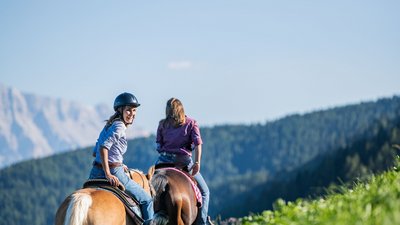 Due donne a cavallo con montagne e bosco sullo sfondo