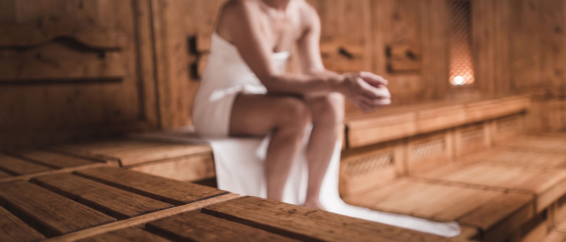 Donna seduta in sauna di legno con asciugamano bianco