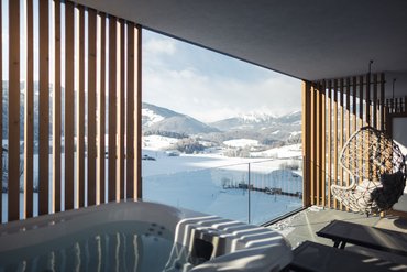Balcony with hot tub and hanging chair overlooking snowy mountains