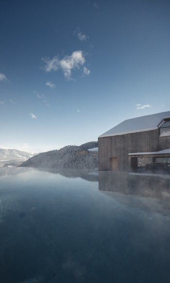 Outdoor pool with mist in front of a house in a snowy mountain landscape