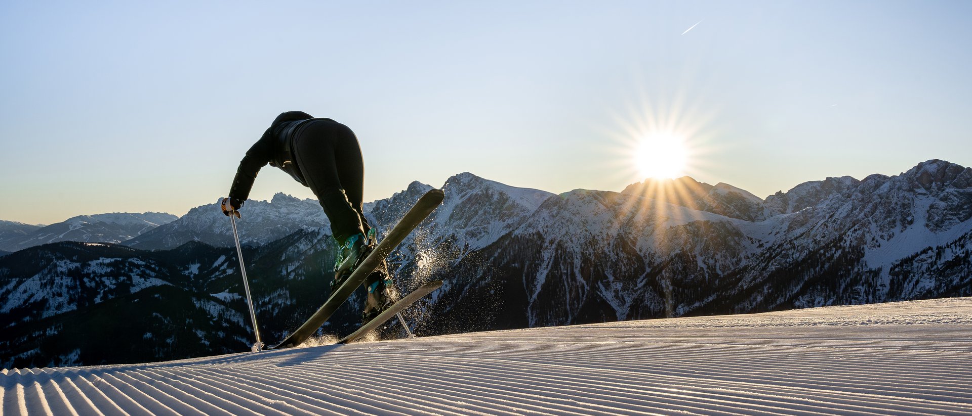 Skifahrer startet auf präparierter Piste bei Sonnenaufgang in den Bergen