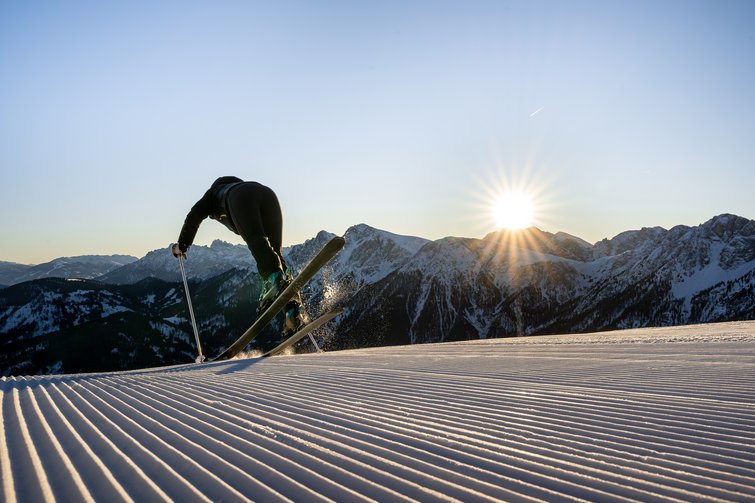 Die Heimat des Strahlens: Ihr Wellnesshotel in Südtirol Skifahrer startet auf präparierter Piste bei Sonnenaufgang in den Bergen