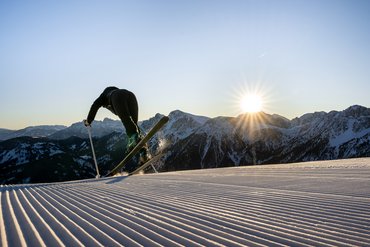 Skifahrer startet auf präparierter Piste bei Sonnenaufgang in den Bergen