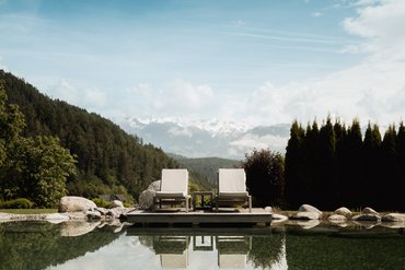 Zwei Liegestühle neben einem klaren Teich mit Bergpanorama im Hintergrund
