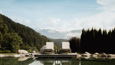 L’esclusività in foto: il nostro chalet in Alto Adige di lusso Due lettini vicino a uno stagno limpido con vista sulle montagne