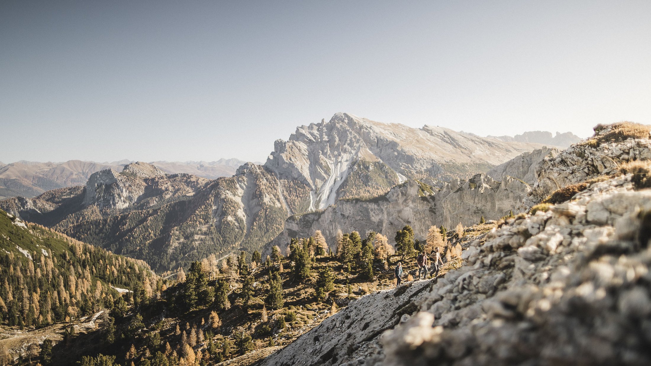 Wanderer auf Bergpfad vor großer Felsformation und Wald