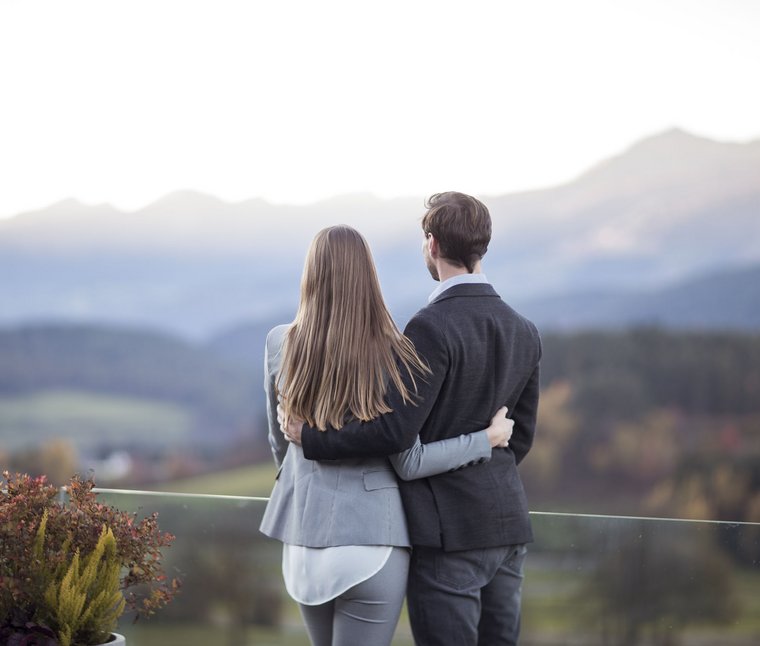 Paar umarmt sich und blickt auf Berglandschaft im Hintergrund