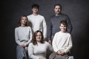 Five family members in front of gray background, three seated in front and two standing