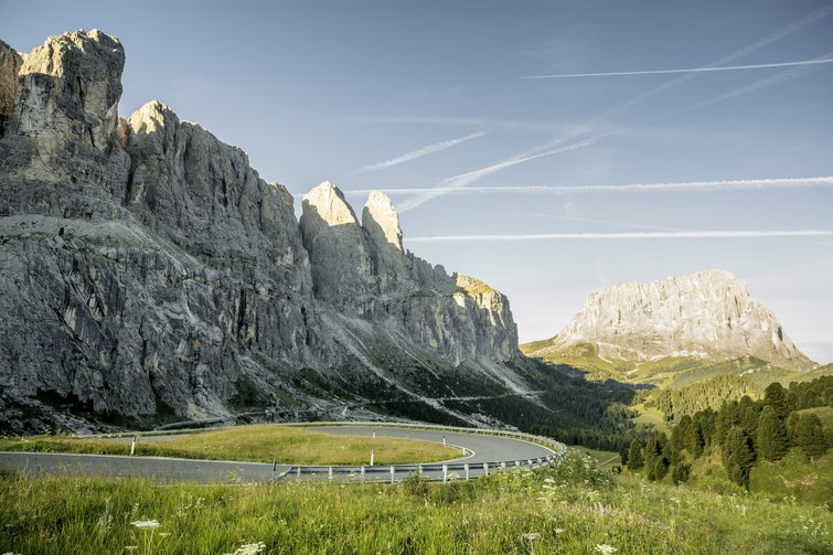 Winding mountain road with rocky peaks and green valley under clear sky