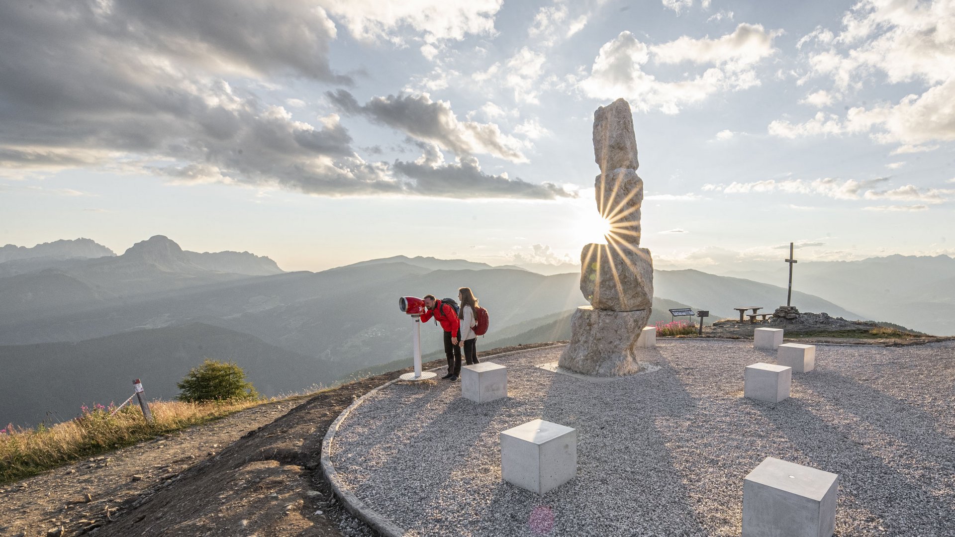 Zwei Personen schauen durch Fernrohr auf Berggipfel mit Sonnenstrahlen
