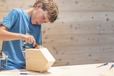Boy focused on carving a wooden object in workshop