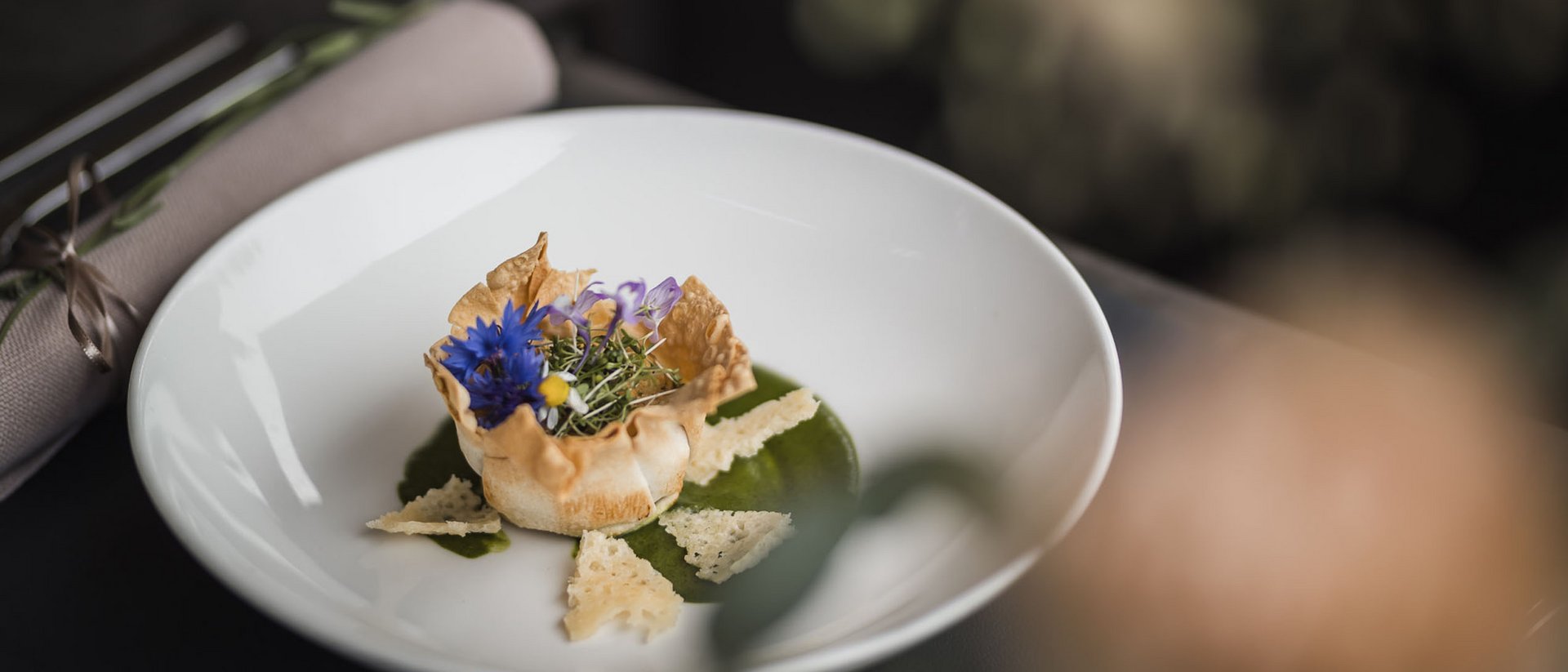 Fein angerichtete Vorspeise mit essbaren Blüten und grüner Sauce auf weißem Teller