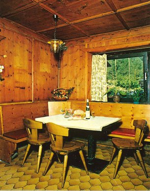 Wood-paneled room with corner bench, three chairs and table set with wine and bread