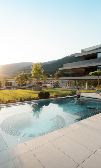 Uomo entra in piscina moderna all'aperto al tramonto in resort di lusso