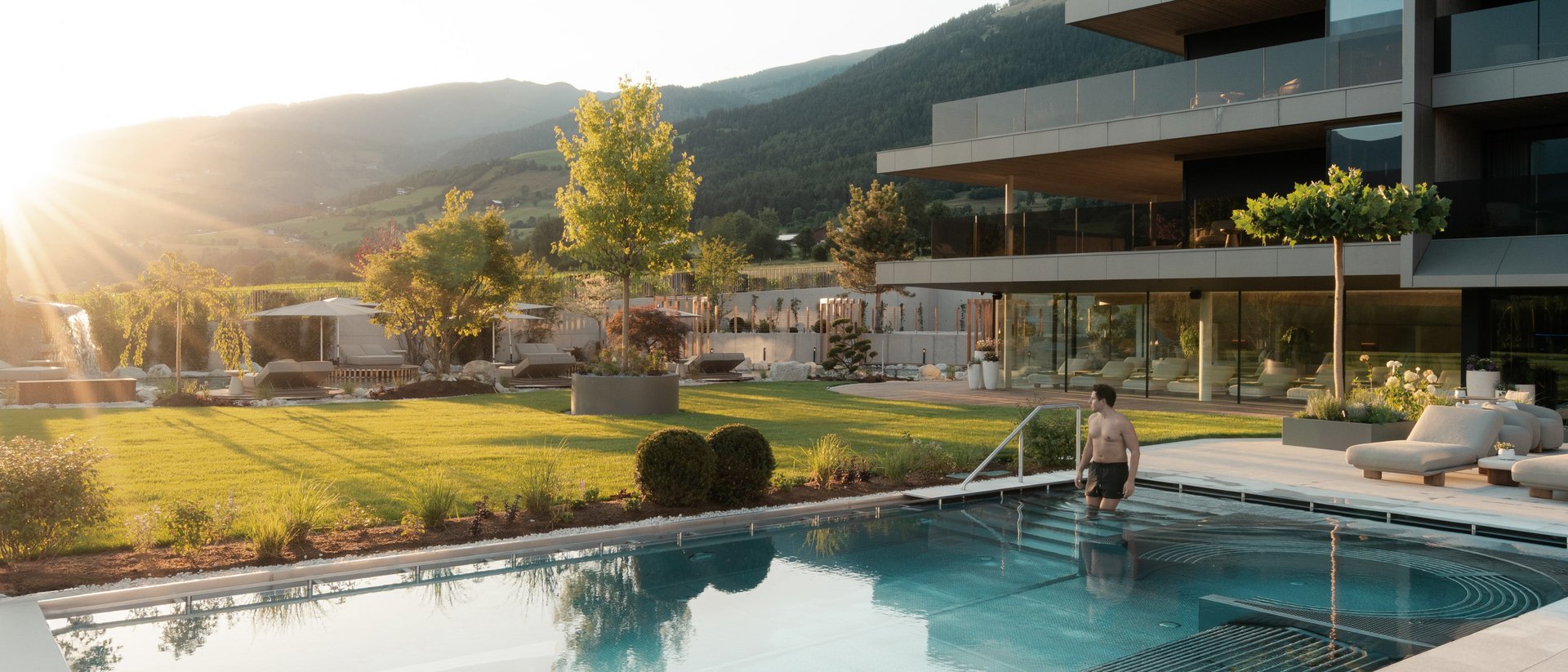 Die Heimat des Strahlens: Ihr Wellnesshotel in Südtirol Mann steigt in modernen Außenpool bei Sonnenuntergang in Luxusresort