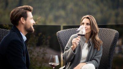 L’esclusività in foto: il nostro chalet in Alto Adige di lusso Coppia che beve vino rosso e chiacchiera all'aperto sulla terrazza.