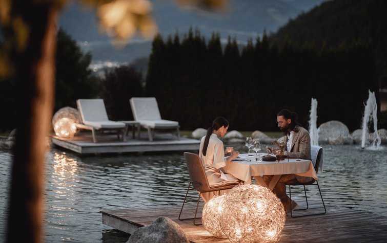 Coppia cena romantica su piattaforma di legno vicino all'acqua con luci decorative