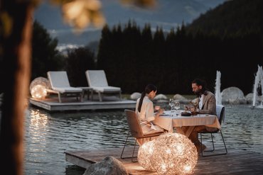 Paar hat romantisches Abendessen auf Holzdeck neben Wasser mit Dekolichter