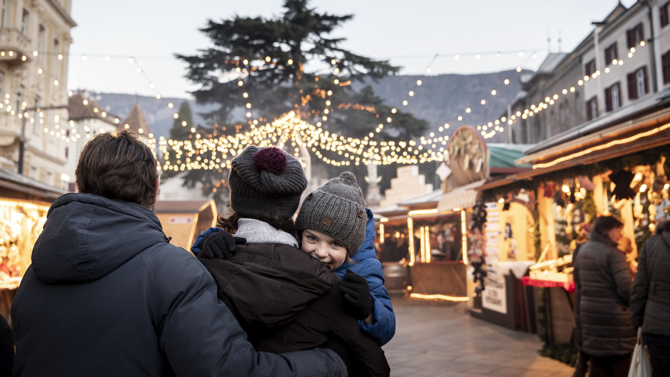 Famiglia al mercatino di Natale con luci e bancarelle al crepuscolo