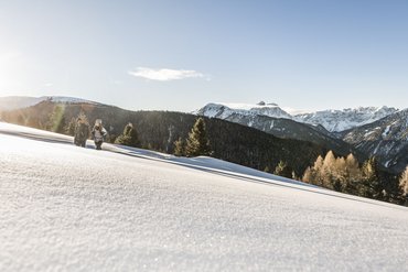 Zwei Wanderer gehen durch verschneite Berglandschaft bei Sonnenschein