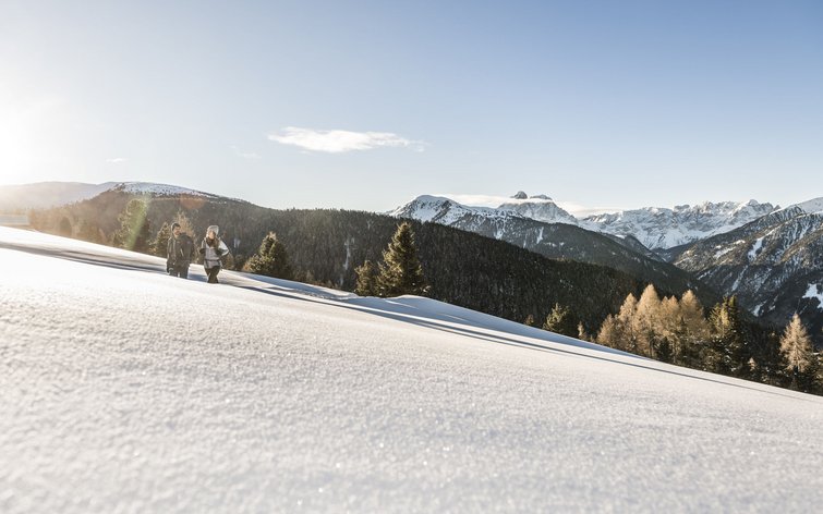 Zwei Wanderer gehen durch verschneite Berglandschaft bei Sonnenschein