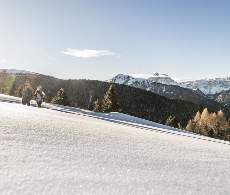 Due escursionisti camminano in un paesaggio montano innevato al sole