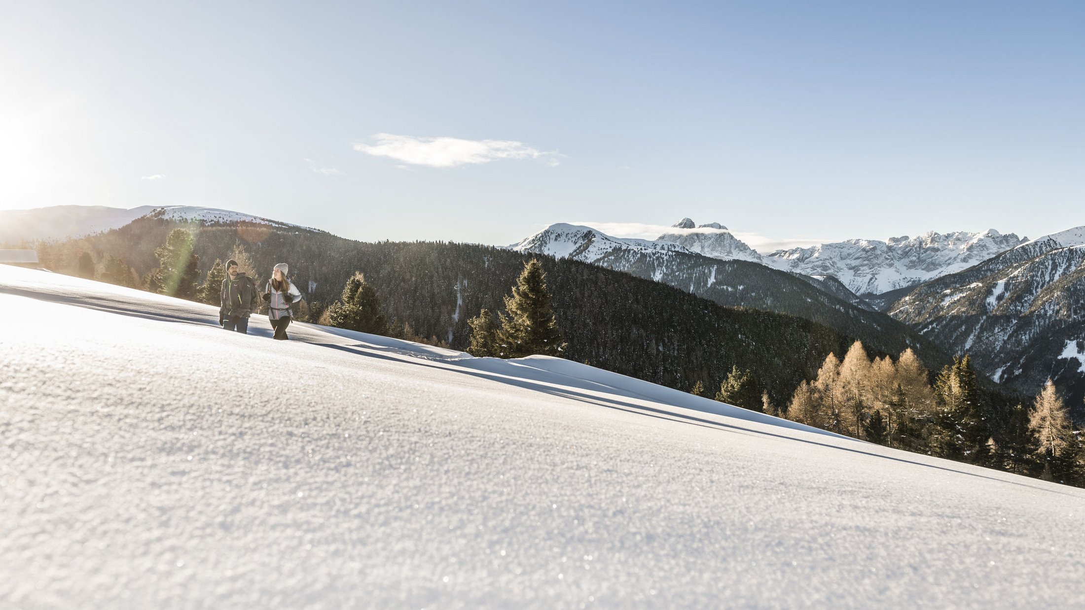 Zwei Wanderer gehen durch verschneite Berglandschaft bei Sonnenschein