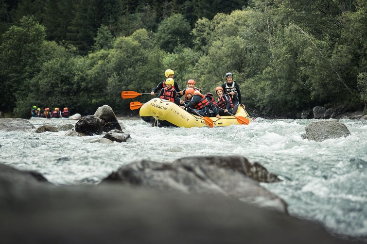 Gruppo che fa rafting in acque bianche con caschi e giubbotti di salvataggio