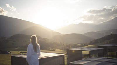 Donna in accappatoio guarda il paesaggio montano soleggiato e piscina