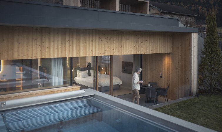 Mann auf Terrasse vor modernem Holzhaus mit Swimmingpool