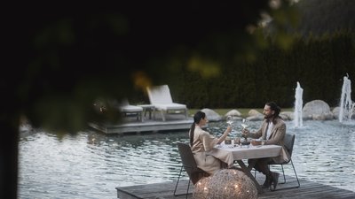 L’esclusività in foto: il nostro chalet in Alto Adige di lusso Coppia brinda con vino a cena vicino a uno stagno con fontane e lanterne.