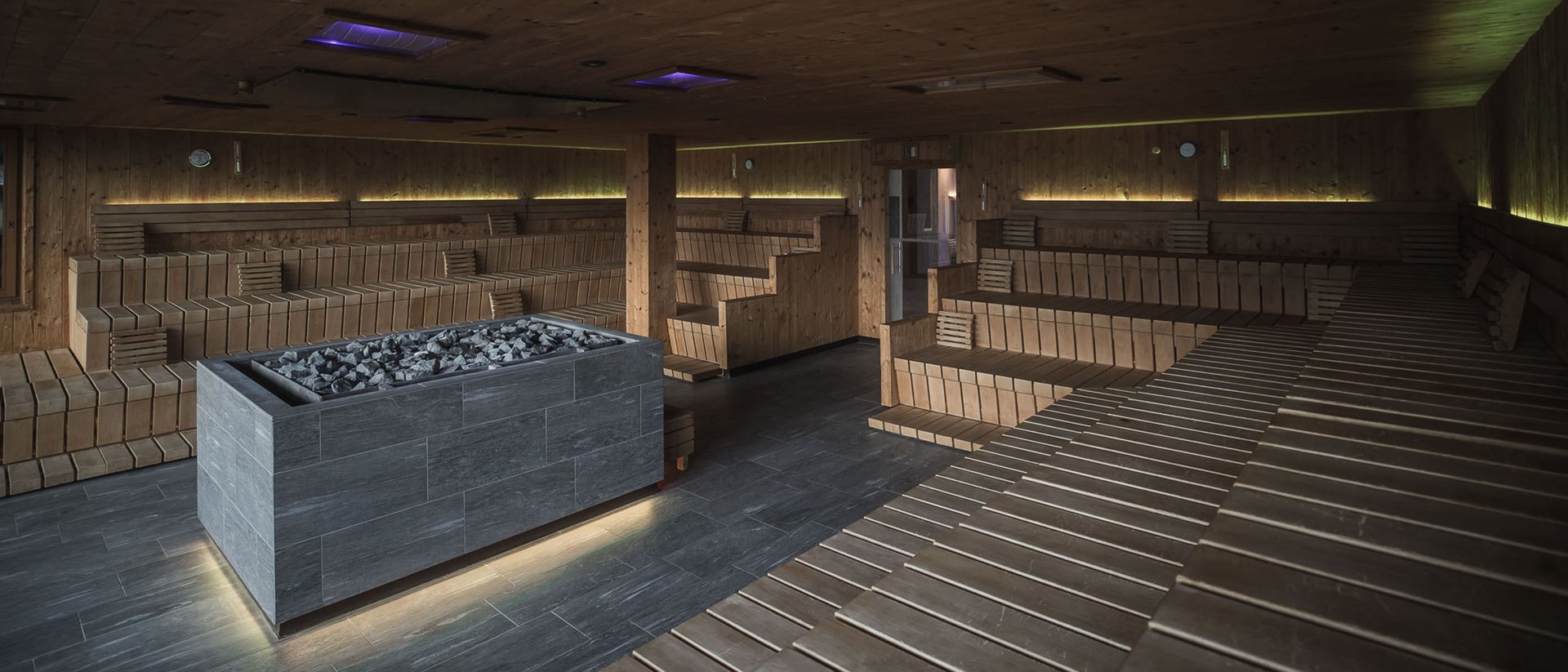 Large wooden room with heated stone fireplace in modern sauna