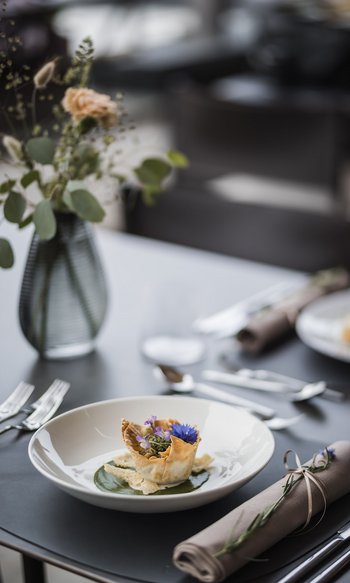 Fein angerichtete Vorspeise mit essbaren Blüten auf weißem Teller