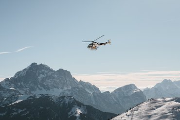 Hubschrauber fliegt über verschneite Berge unter klarem Himmel