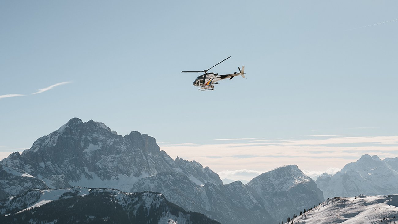 Hubschrauber fliegt über verschneite Berge unter klarem Himmel