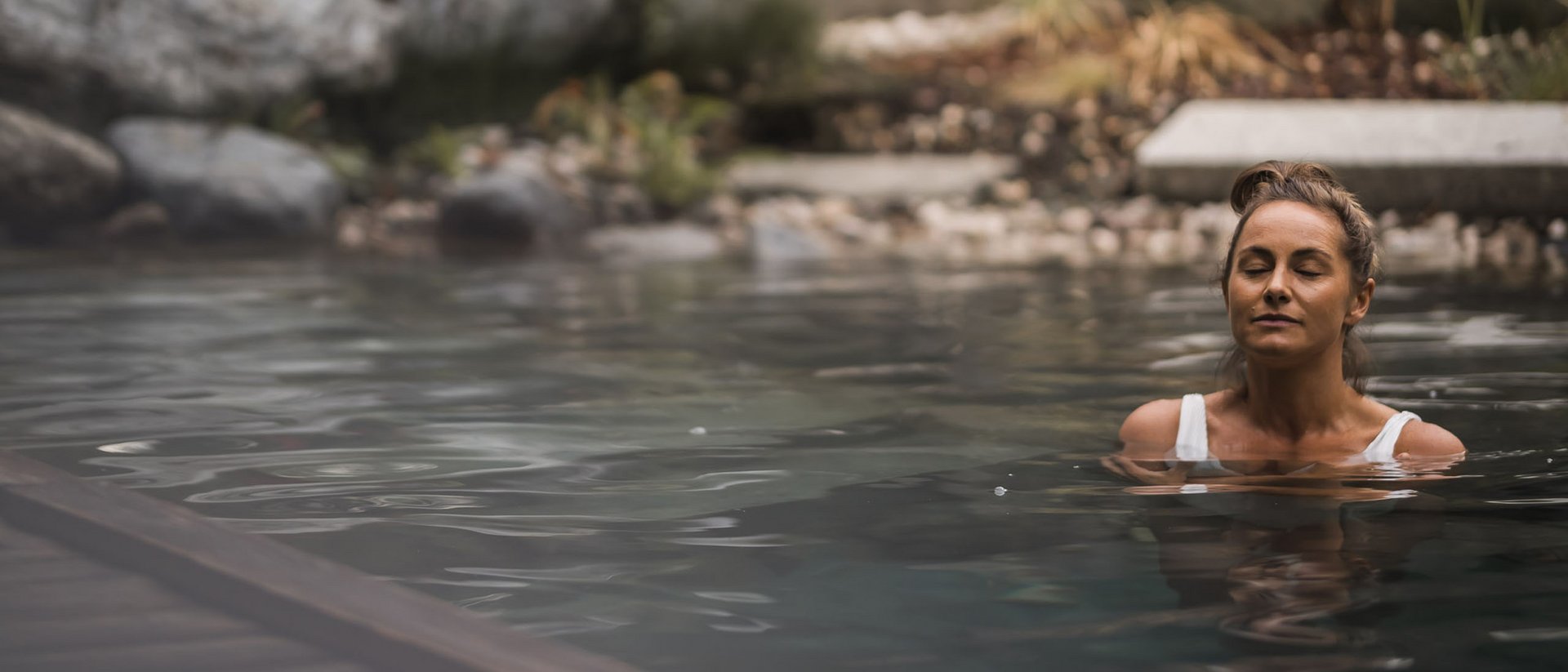 Frau entspannt im Wasser eines Pools mit Steinen im Hintergrund