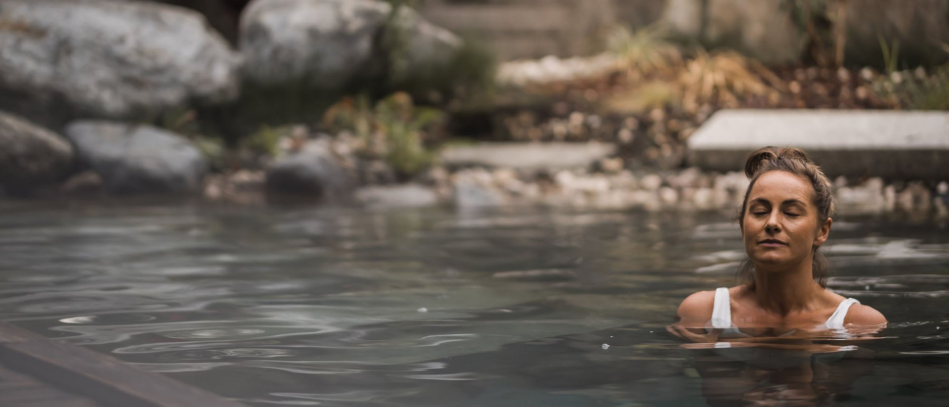 Frau entspannt im Wasser eines Pools mit Steinen im Hintergrund