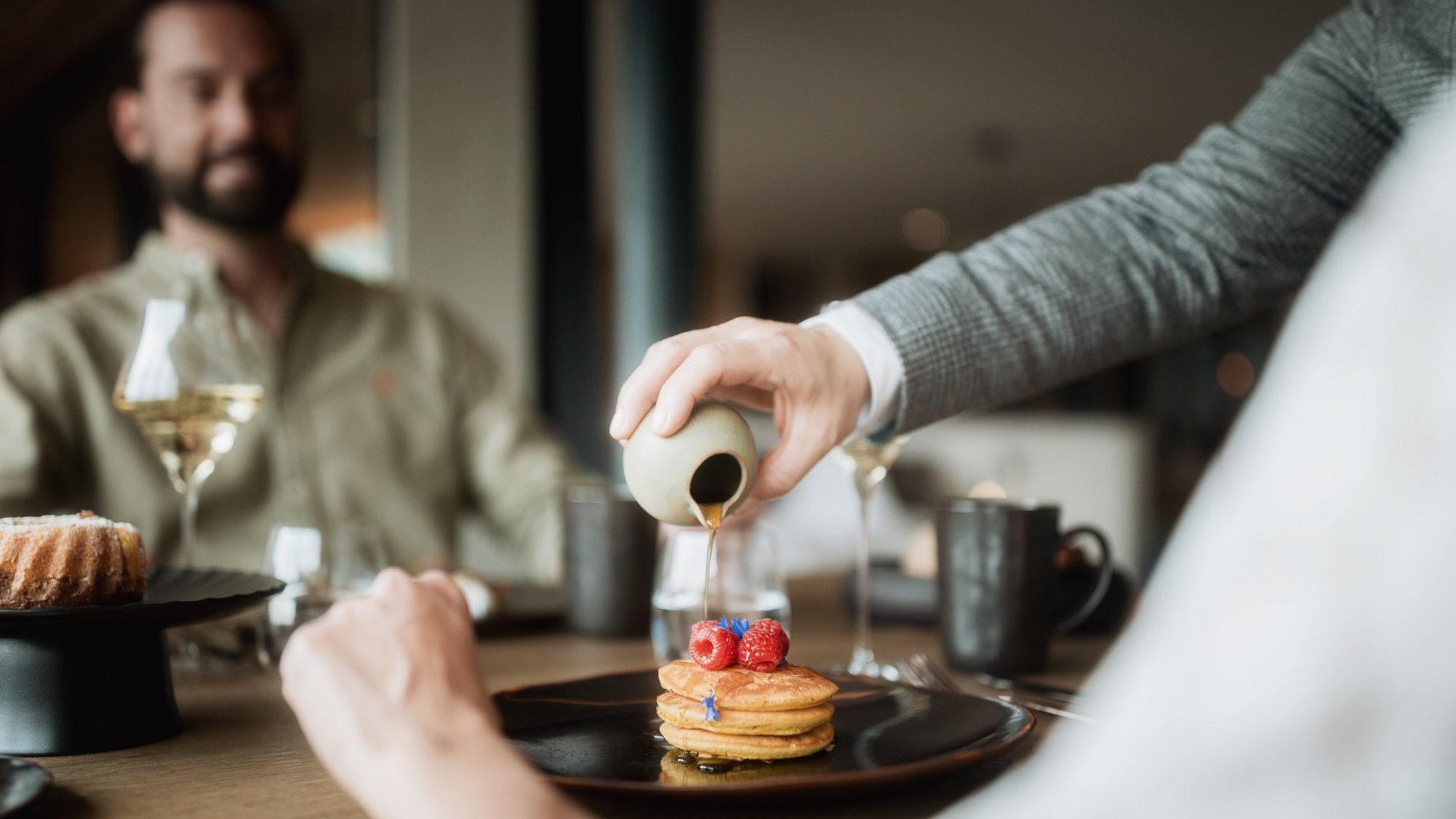 Sirup wird auf Pancakes mit Beeren und Blumen in einem Restaurant gegossen