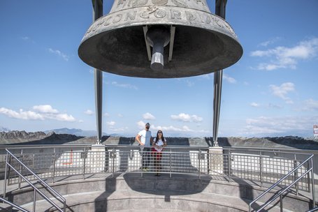 Large bell on platform with two people and mountain landscape in background