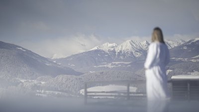 Donna in accappatoio che guarda le montagne innevate e foreste