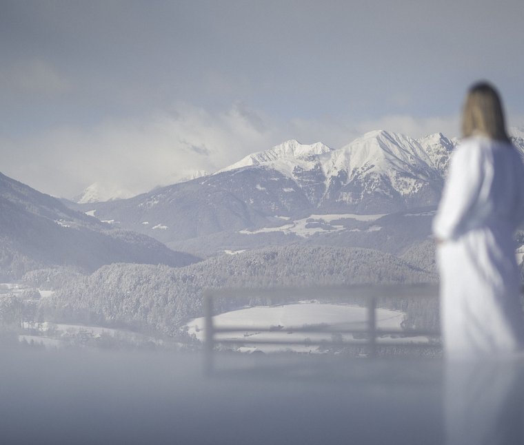 Donna in accappatoio che guarda le montagne innevate e foreste