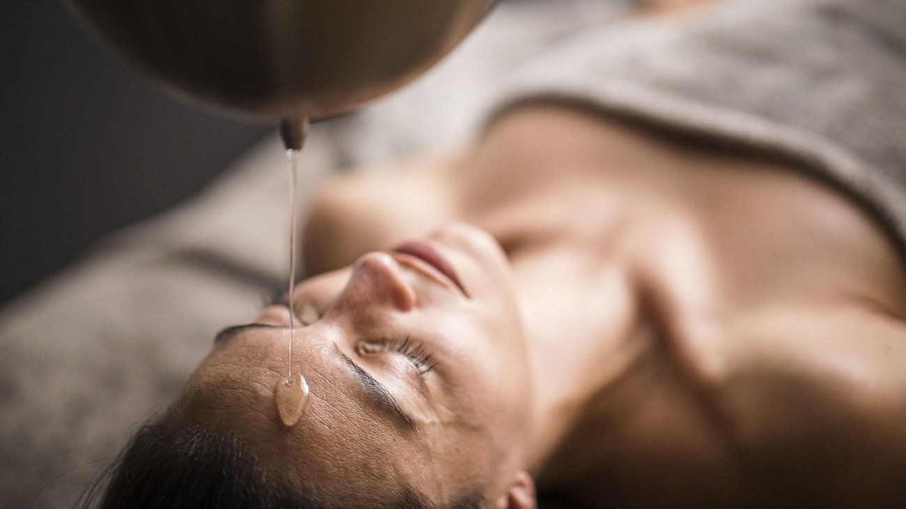 Frau erhält Ayurveda-Ölguss-Therapie auf der Stirn