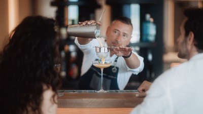 Bartender straining and pouring cocktail into glass in front of guests