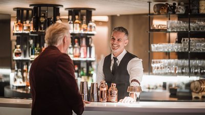Bartender in abito sorride a un cliente in un bar moderno